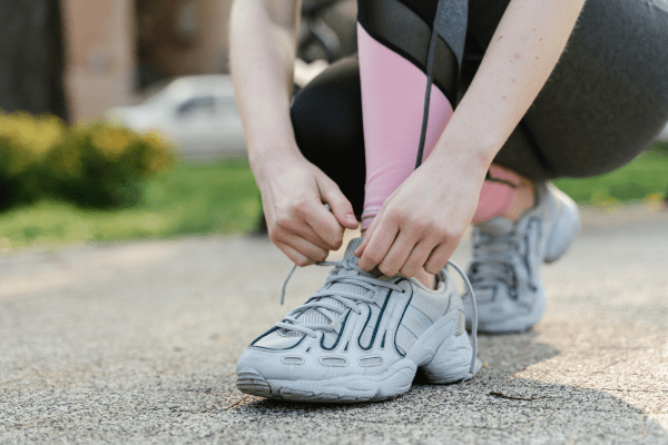 A person outdoors tying athletic sneakers featuring the traditional X-shaped criss-cross lacing style.