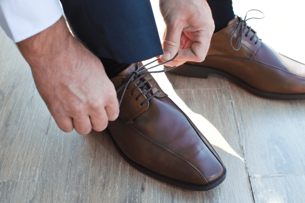 Man tying brown dress shoes using the clean bar lacing style, ideal for formal wear.