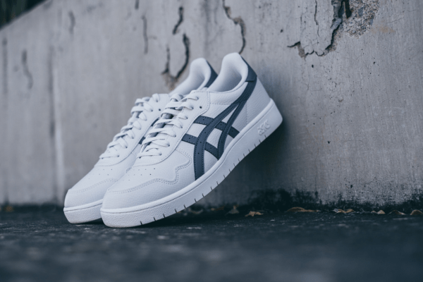 A pair of white sneakers with clean white shoelaces resting against a concrete wall
