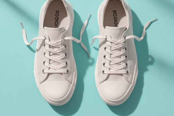 A pair of white canvas shoes with loose laces on a light blue background.